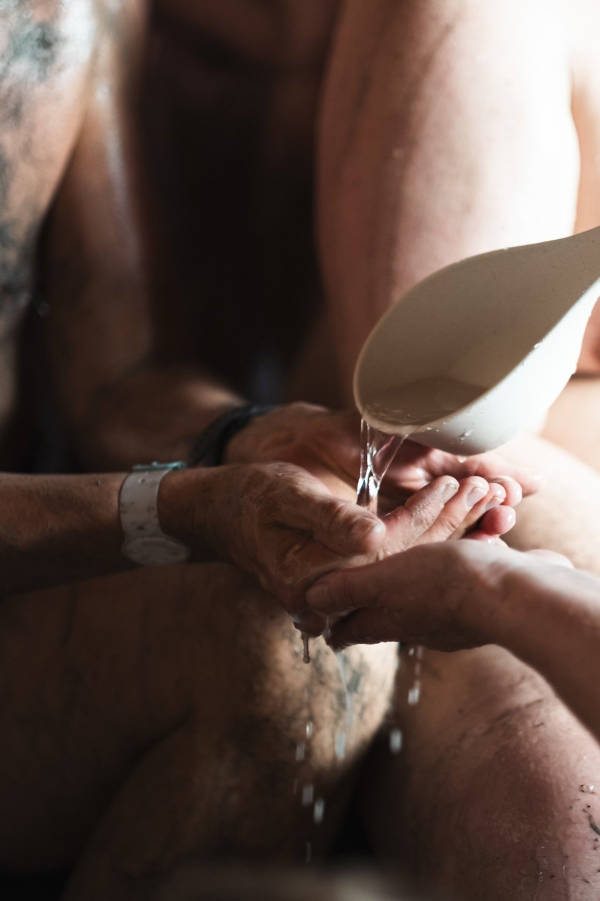 Water poured over cupped hands in a sauna, a moment of care between bathers